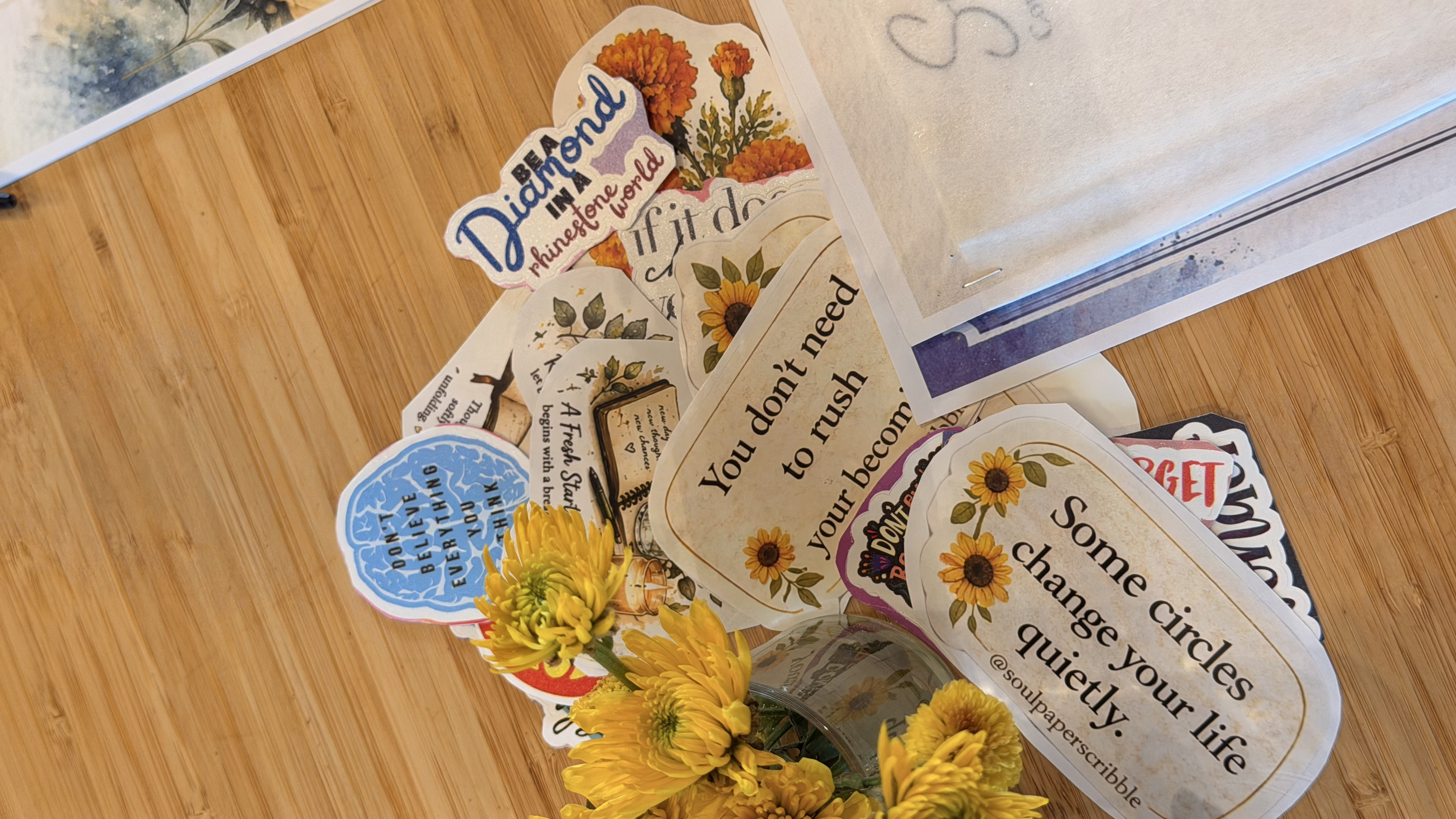 A pile of motivational stickers with yellow flowers on a wooden table.